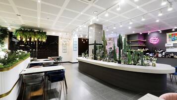 Un interior moderno con mostrador de recepción, zona de estar y plantas decorativas.