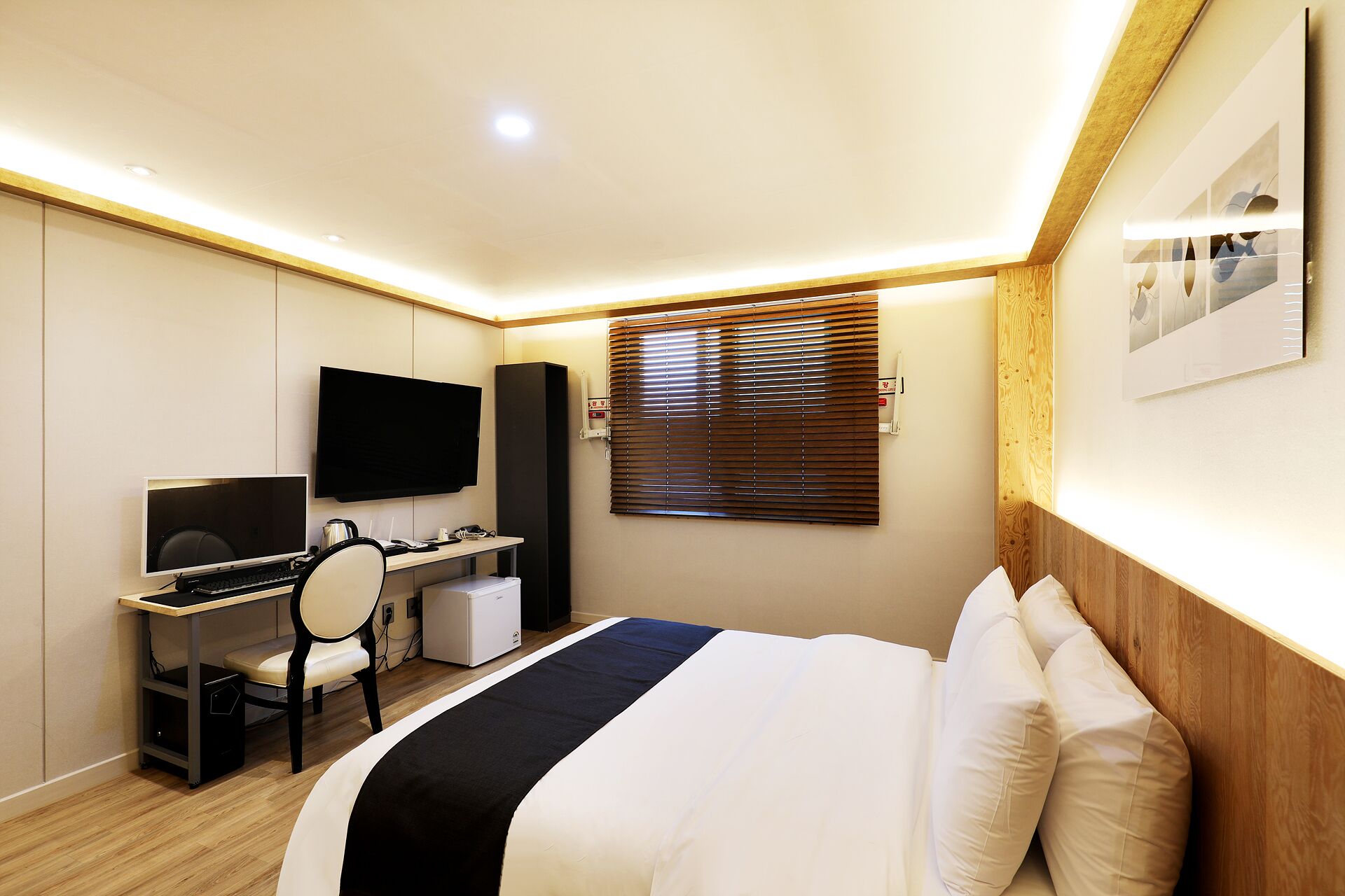 A hotel room with a bed, a desk with a computer, a TV, and a window with blinds.