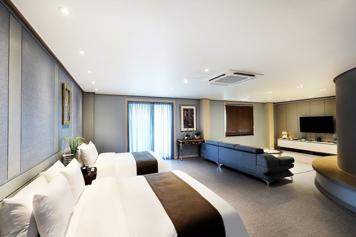A modern hotel room with a large bed, a sofa, a desk, and a TV.