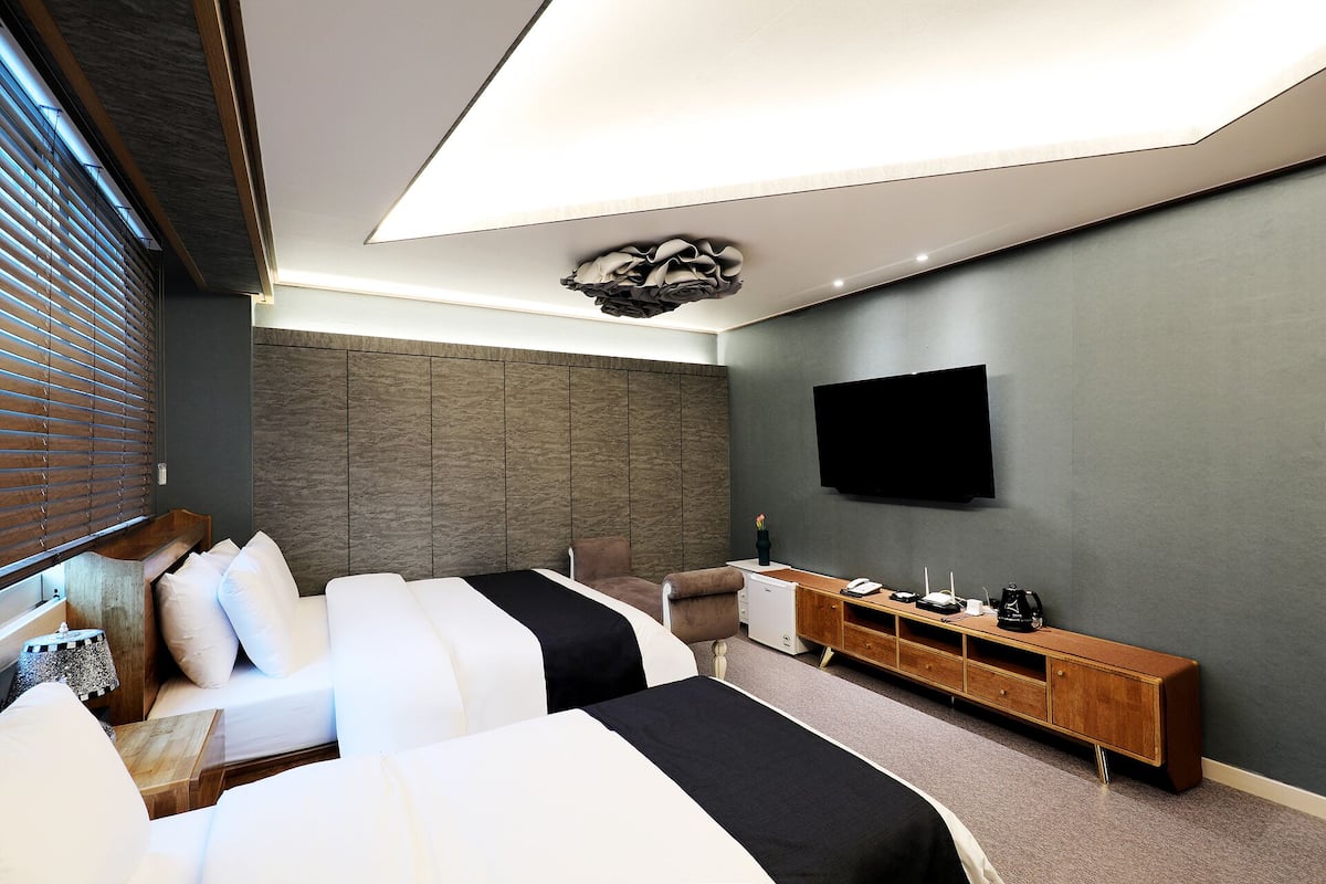 A modern hotel room with two beds, a TV, a wooden console, and a stone-textured wall.