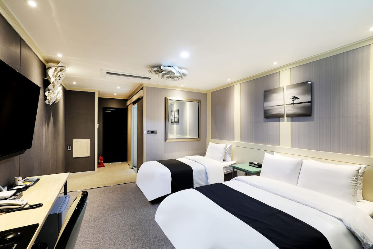 A hotel room with two beds, a desk with a computer, a flat-screen TV, and a wall-mounted mirror.