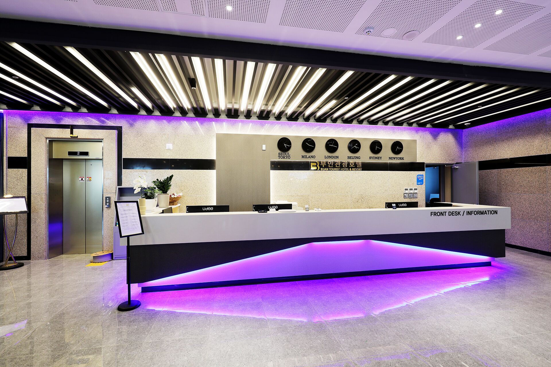 A reception desk with a modern design, a clock displaying multiple time zones, and a sign indicating the hotel is a tourist hotel and resort.