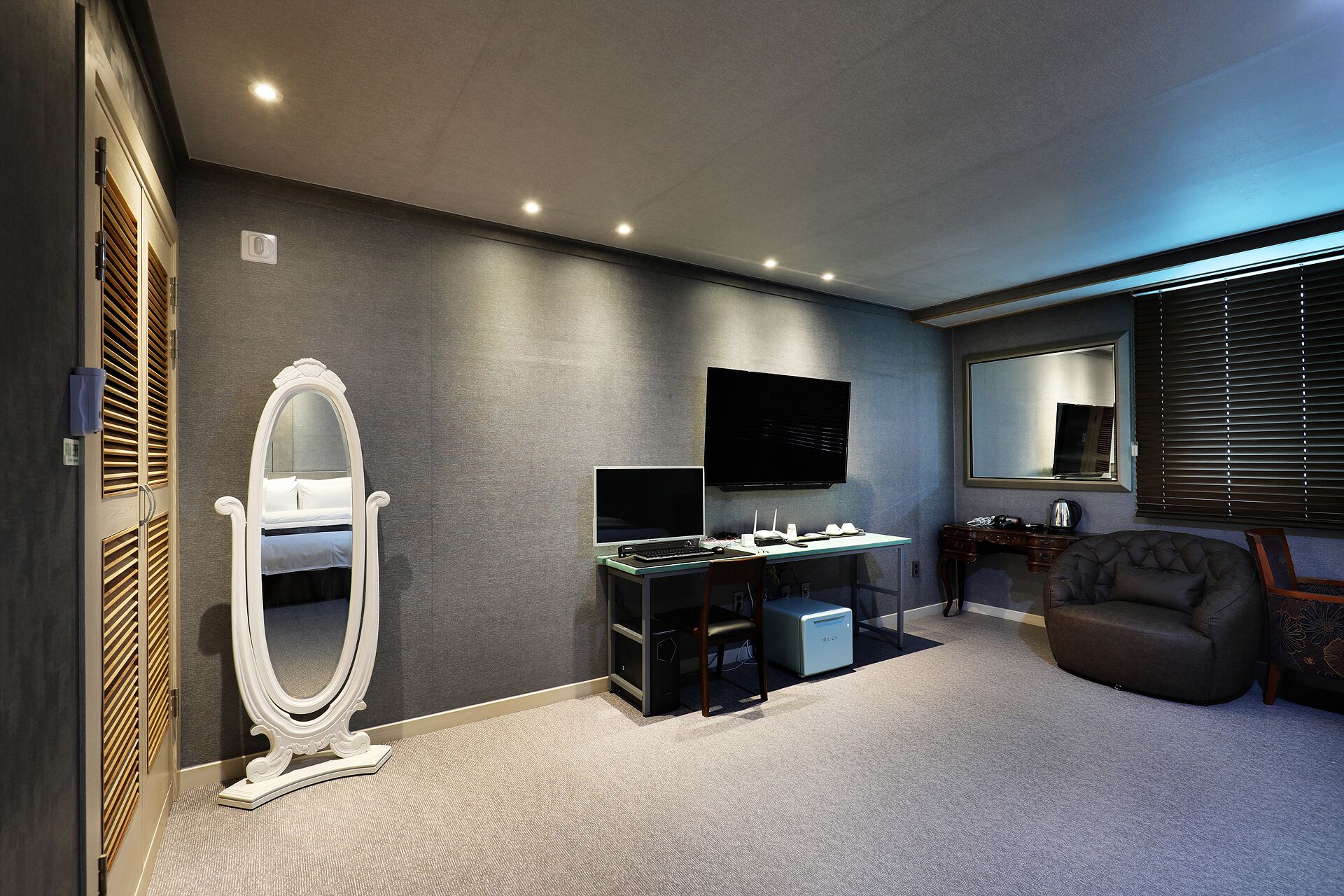 A modern bedroom with a large bed, a desk with a computer, a TV, and a chair.