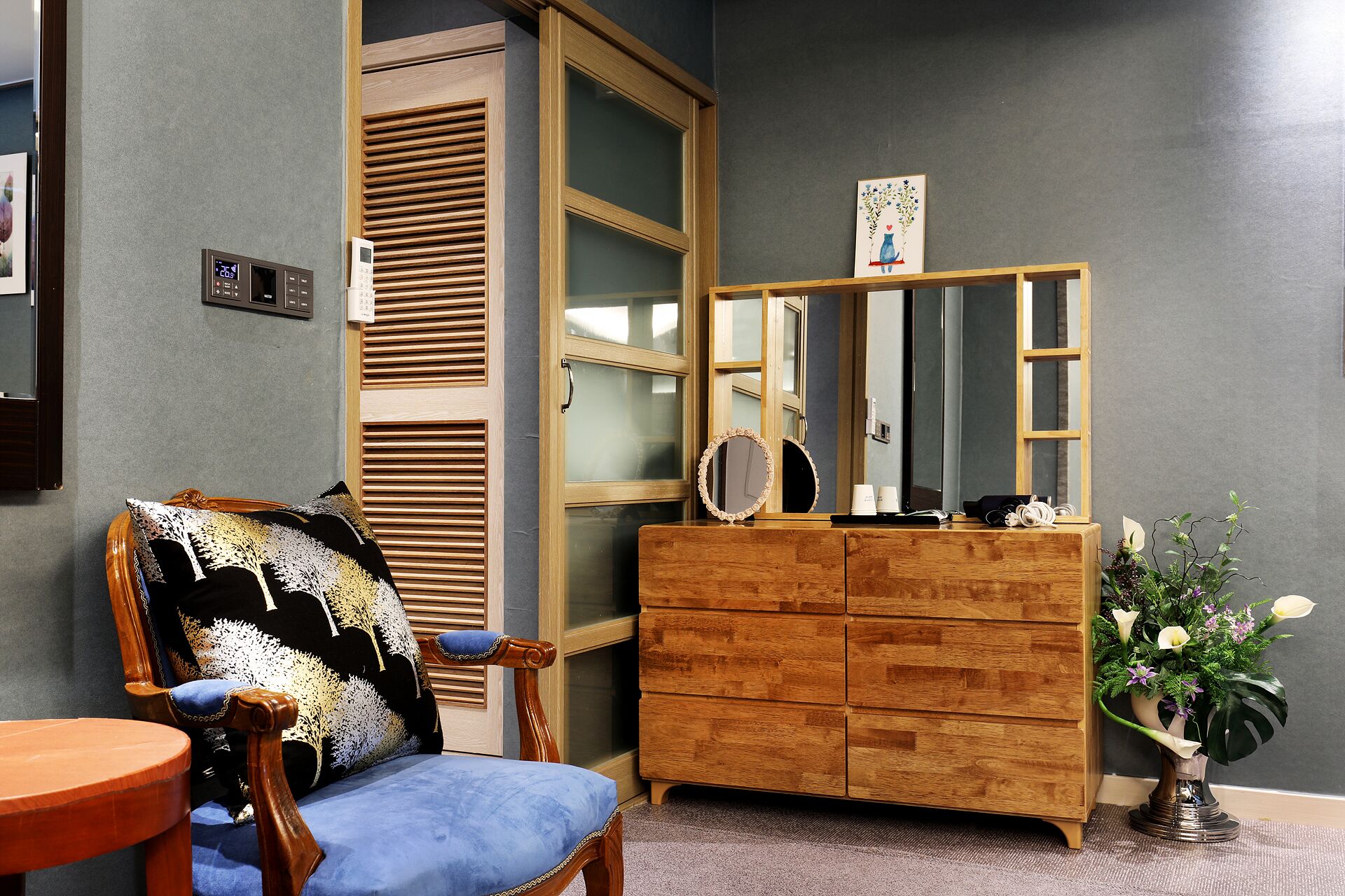 A room with a wooden dresser, a chair with a patterned cushion, a mirror, and a small table.