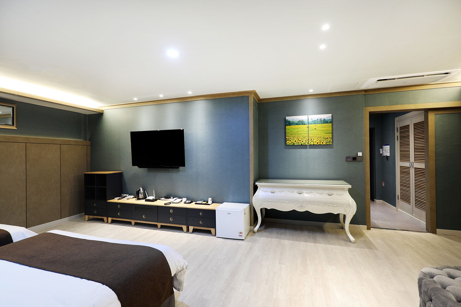 A hotel room with a bed, a desk with a flat-screen TV, a small table, and a wall-mounted picture.
