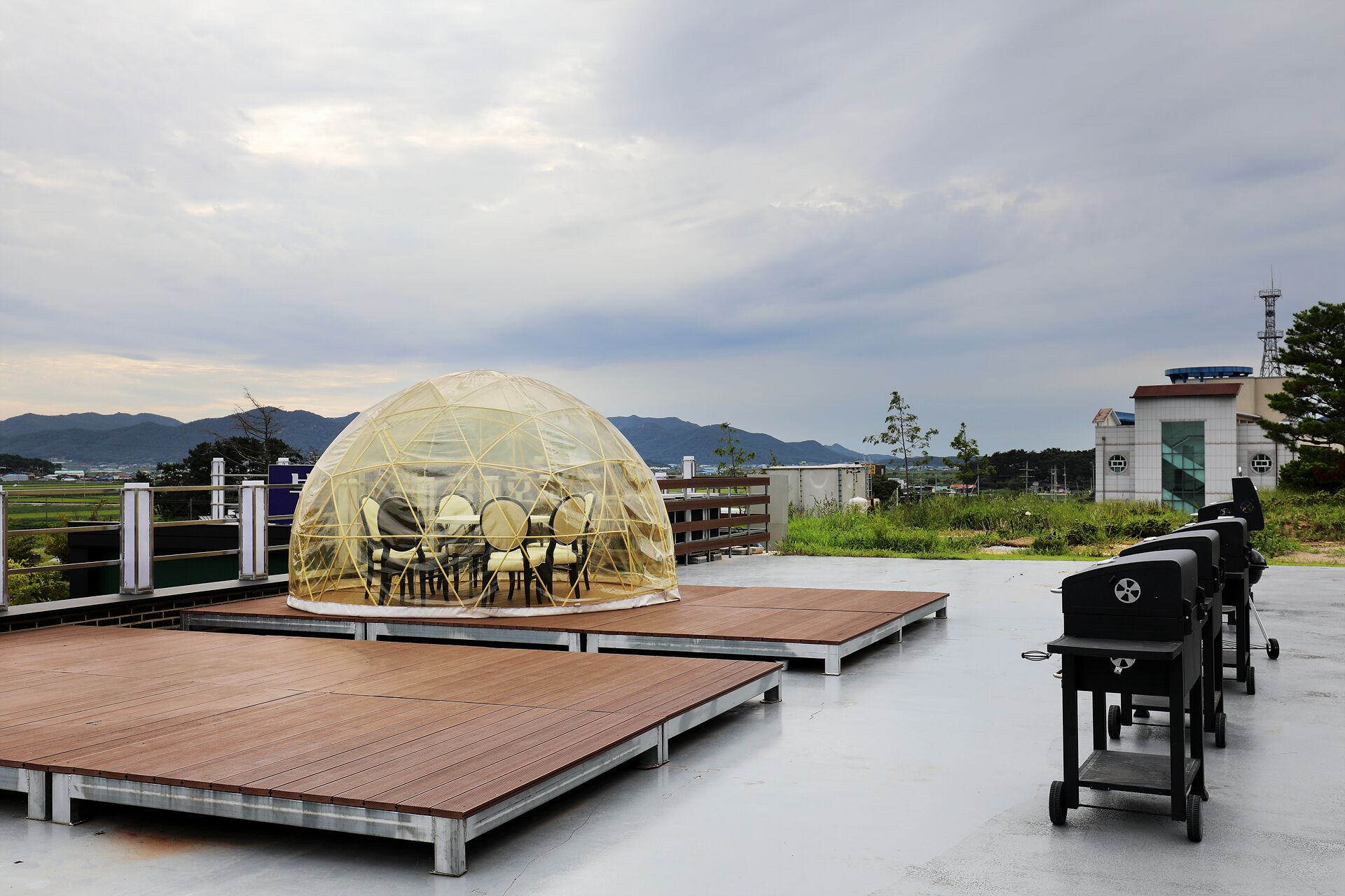 A rooftop terrace with a transparent dome seating area, a barbecue grill, and a view of mountains.