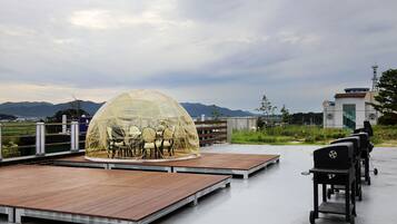A rooftop terrace with a transparent dome seating area, a barbecue grill, and a view of mountains.