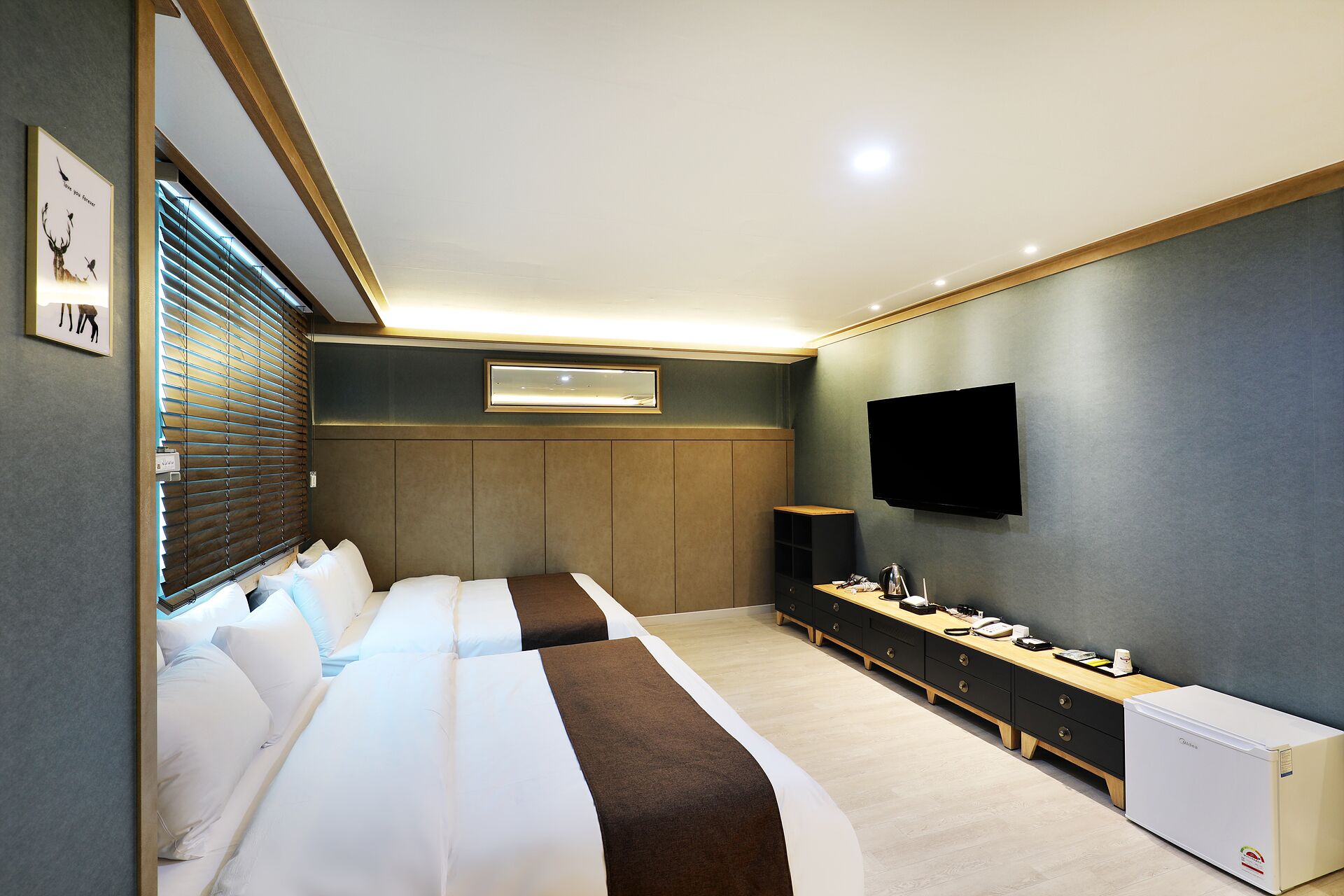 Quarto de hotel moderno com uma cama grande, televisão, minibar e escrivaninha.