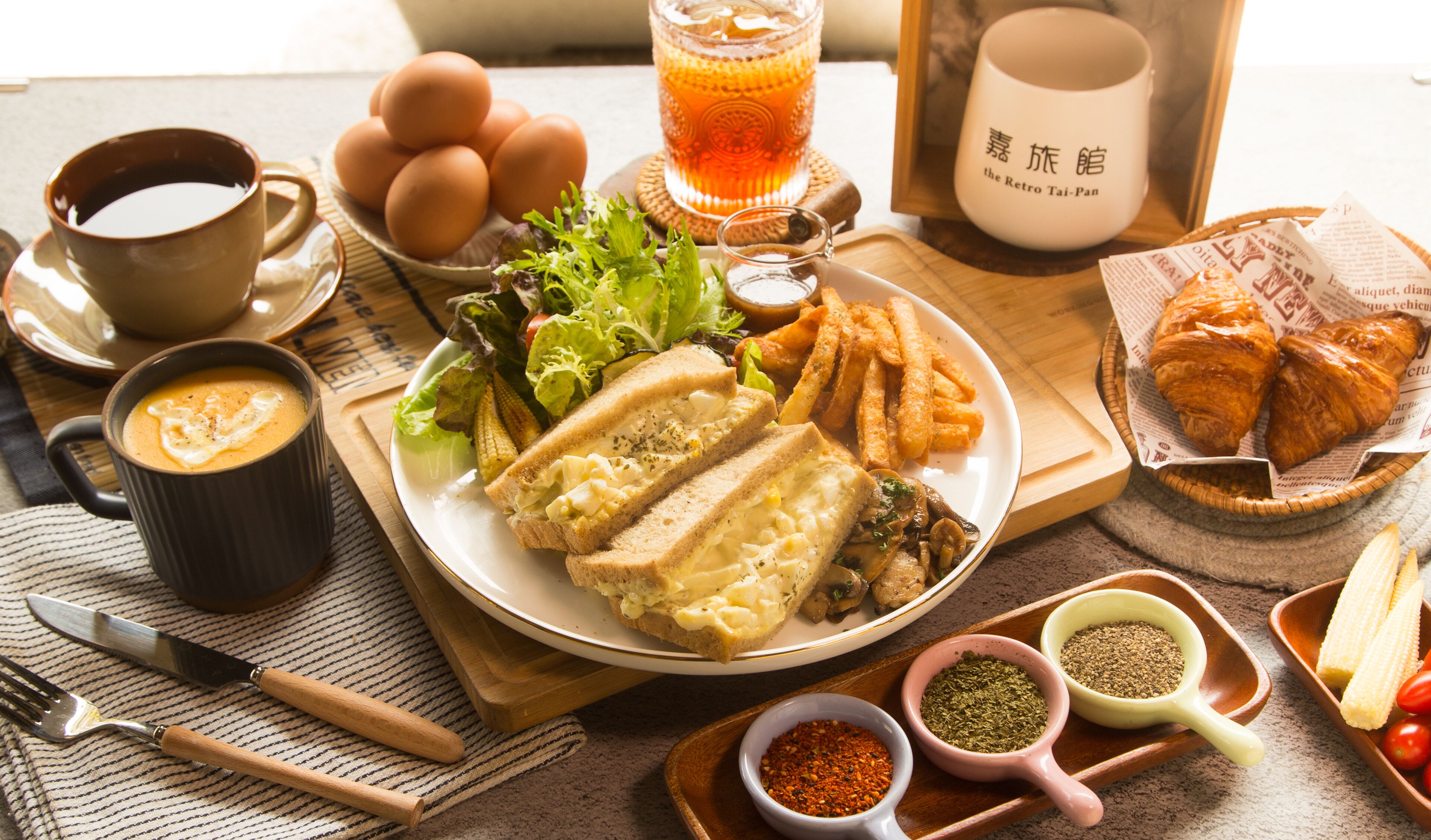 Una mesa de desayuno con huevos, tostadas, ensalada, papas fritas y una taza de té.