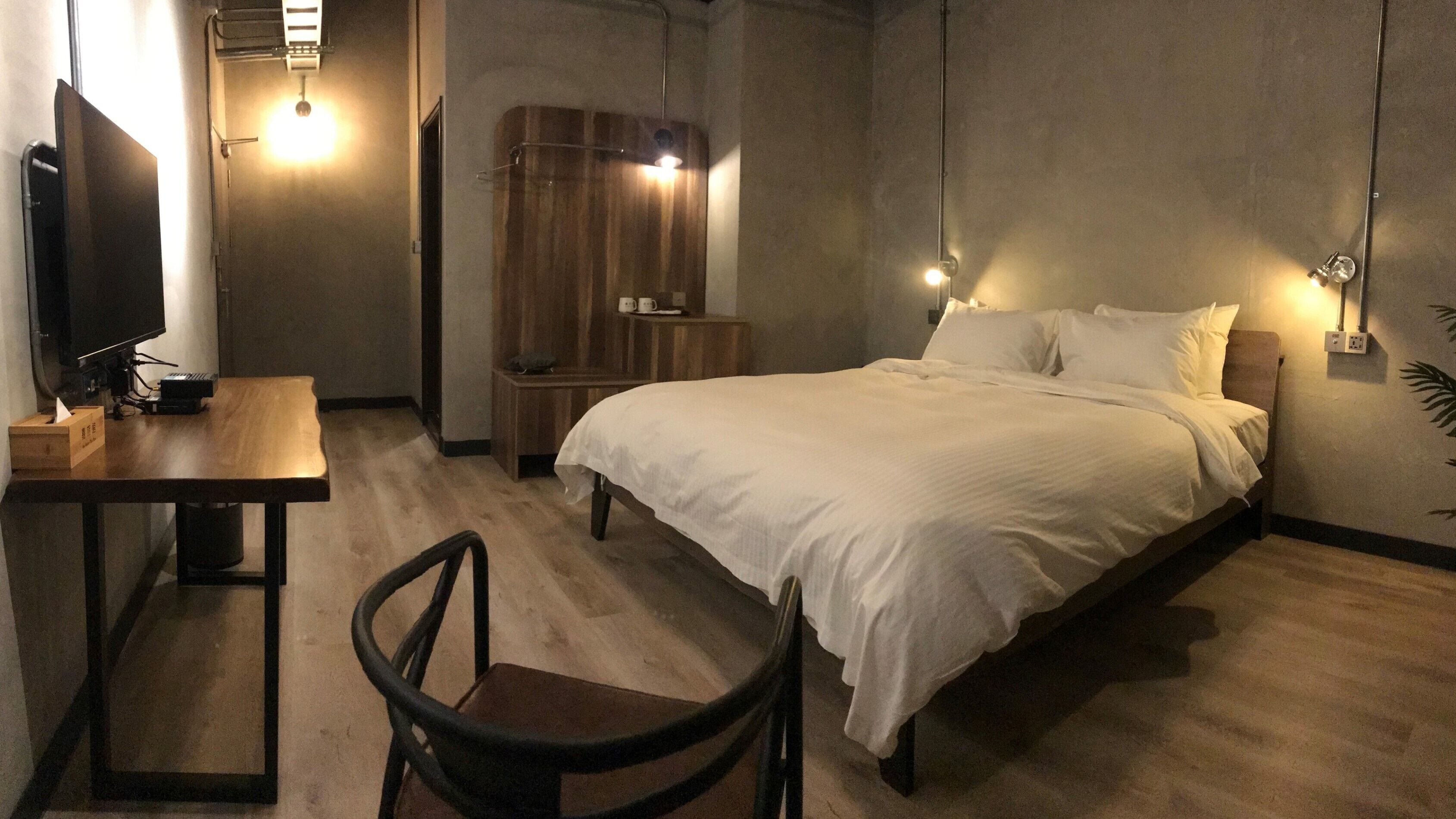 A hotel room with a bed, a desk with a computer, a chair, and a wardrobe.