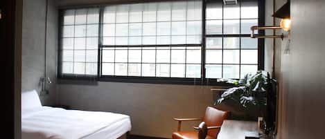 A room with a bed, a desk, a chair, and a large window with blinds.