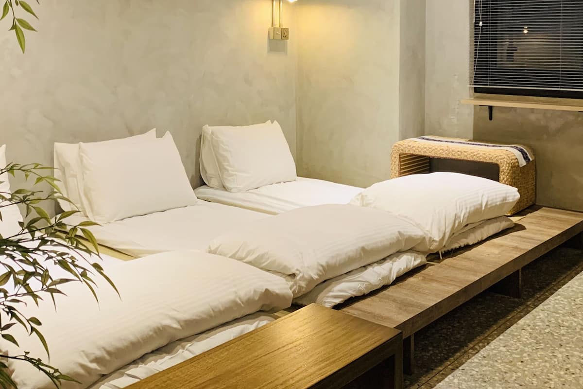 Quarto minimalista com duas camas, uma mesinha de cabeceira, um cesto trançado e uma luminária fixada na parede.