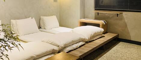 Un dormitorio minimalista con dos camas, una mesita de noche, una cesta tejida y una lámpara de pared.