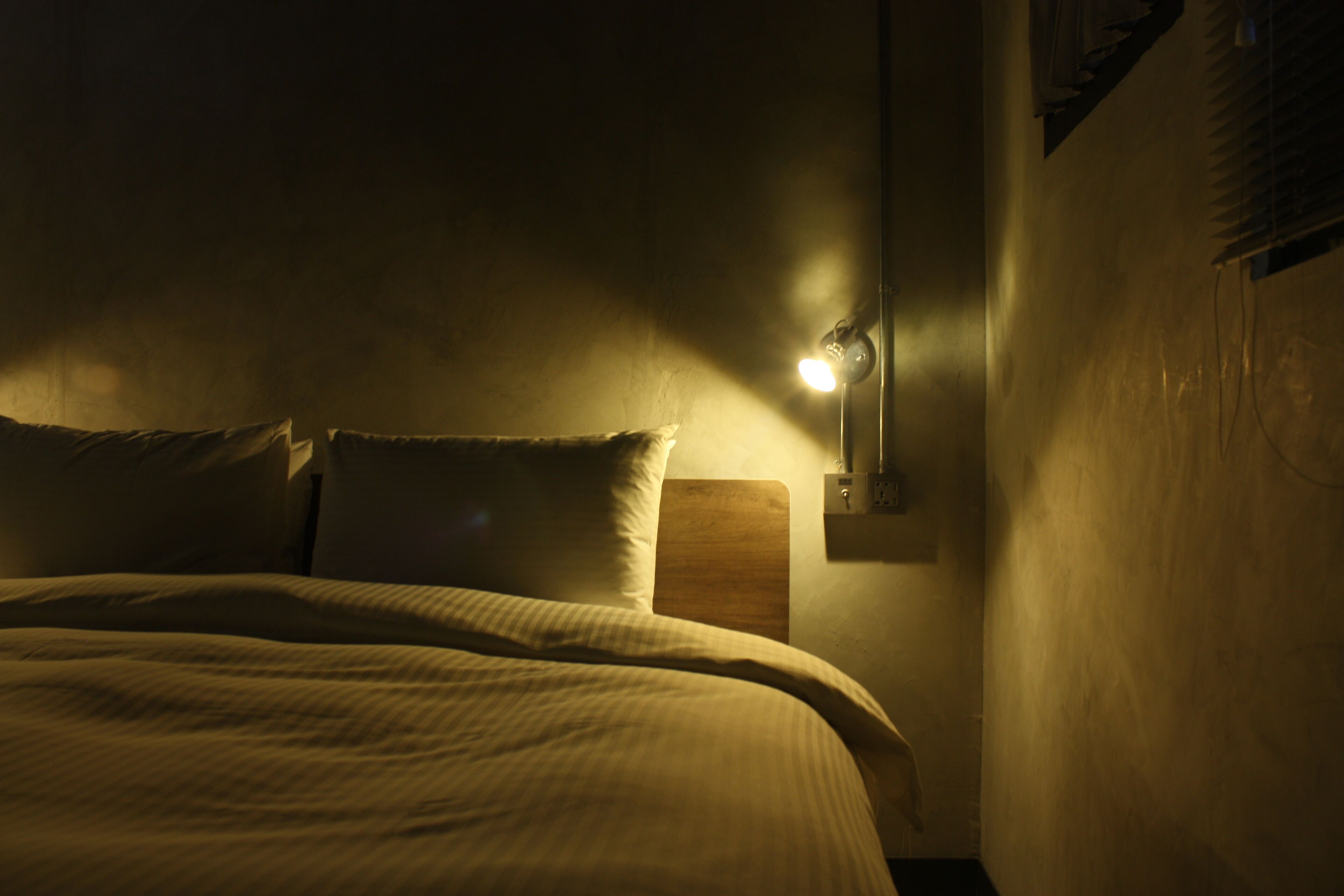 Una habitación tenuemente iluminada con una cama, una mesita de noche y una lámpara de pared.
