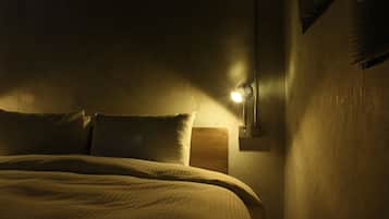 A dimly lit room with a bed, a nightstand, and a wall-mounted lamp.