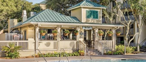Guests can relax on the covered porch with outdoor seating, adjacent to a swimming pool.