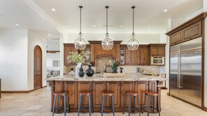Una cocina amplia con una isla grande, armarios de madera, electrodomésticos de acero inoxidable e iluminación colgante.