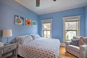 A bedroom with a large bed, two windows, a bedside table with a lamp, and a chair. - Louisville Home w/ Hot Tub in The Highlands! (Louisville)