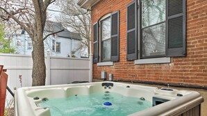 Een jacuzzi in een achtertuin met een bakstenen muur en een witte schutting.
