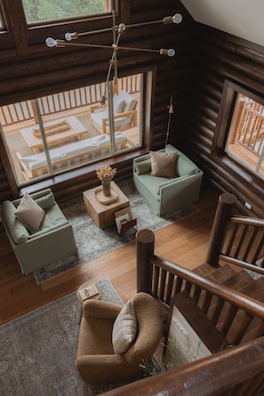 A cozy log cabin interior with a wooden staircase, a green sofa, a brown armchair, and a wooden coffee table.