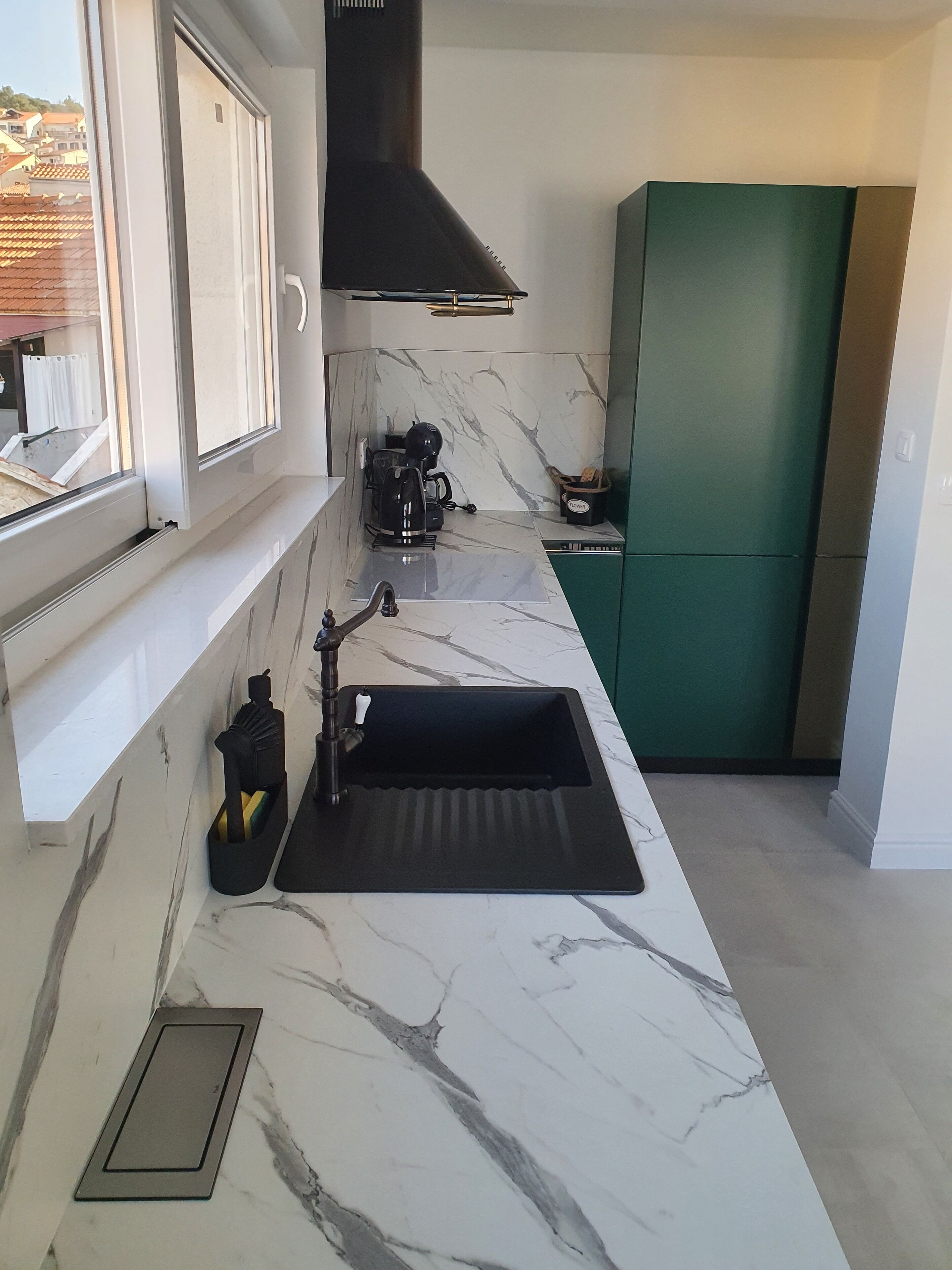 A modern kitchen with a black sink, a coffee maker, and a green cabinet.