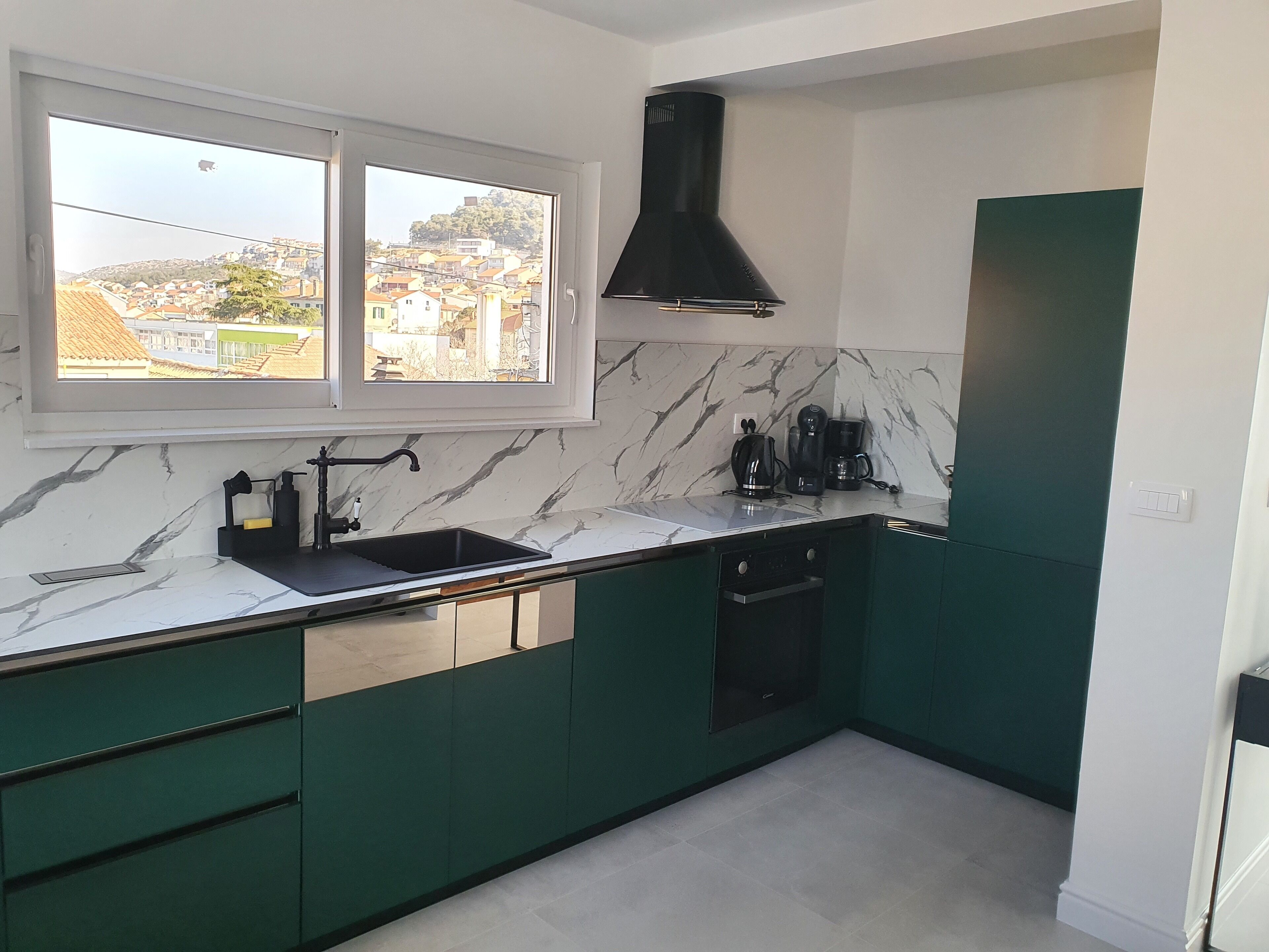 A kitchen with a black range hood, a sink, and a window overlooking a cityscape.