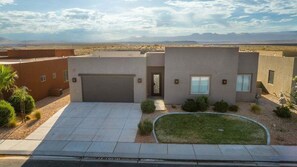 A modern house with a garage, a small lawn, and a desert landscape in the background. - Chandler: Private Swim Spa + Golf + Sand Dunes (Hurricane)