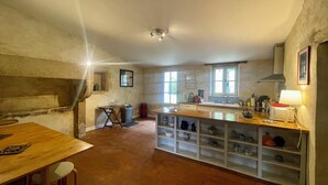 A rustic kitchen with a wooden table, a built-in shelf with kitchenware, and a window providing natural light.