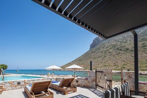Ein Poolbereich mit Liegestühlen, Sonnenschirmen und Blick auf das Meer und die Berge.