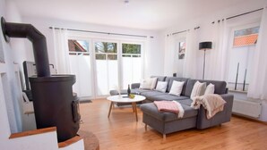 Een woonkamer met een open haard, een grijze bank, een ronde salontafel en een groot raam.