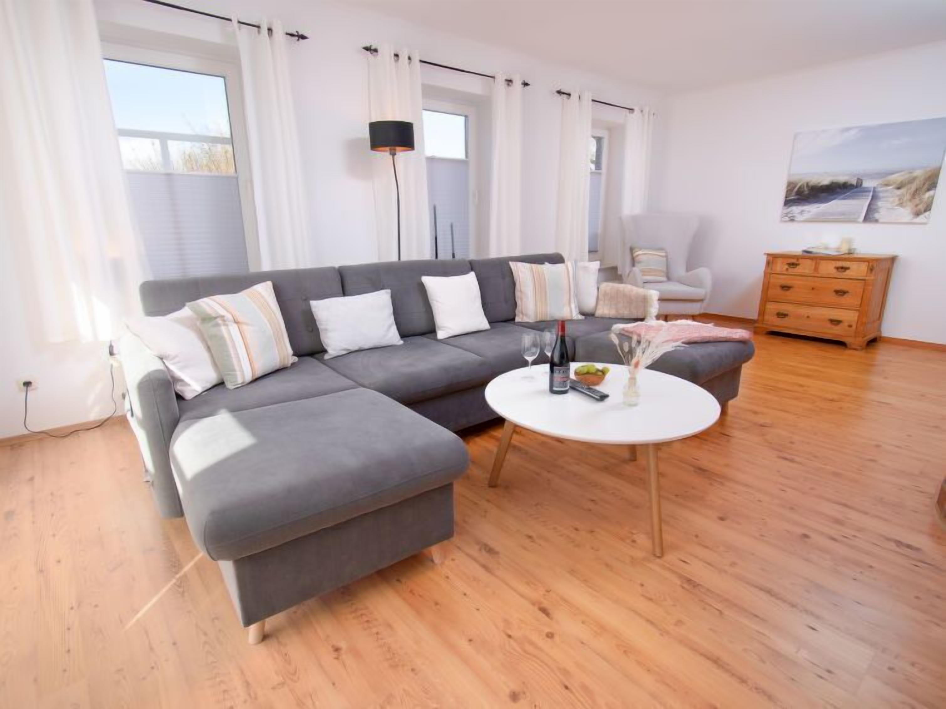 Een moderne woonkamer met een grijze hoekbank, een ronde salontafel en een houten vloer.