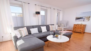 Een moderne woonkamer met een grijze hoekbank, een ronde salontafel en een houten vloer.