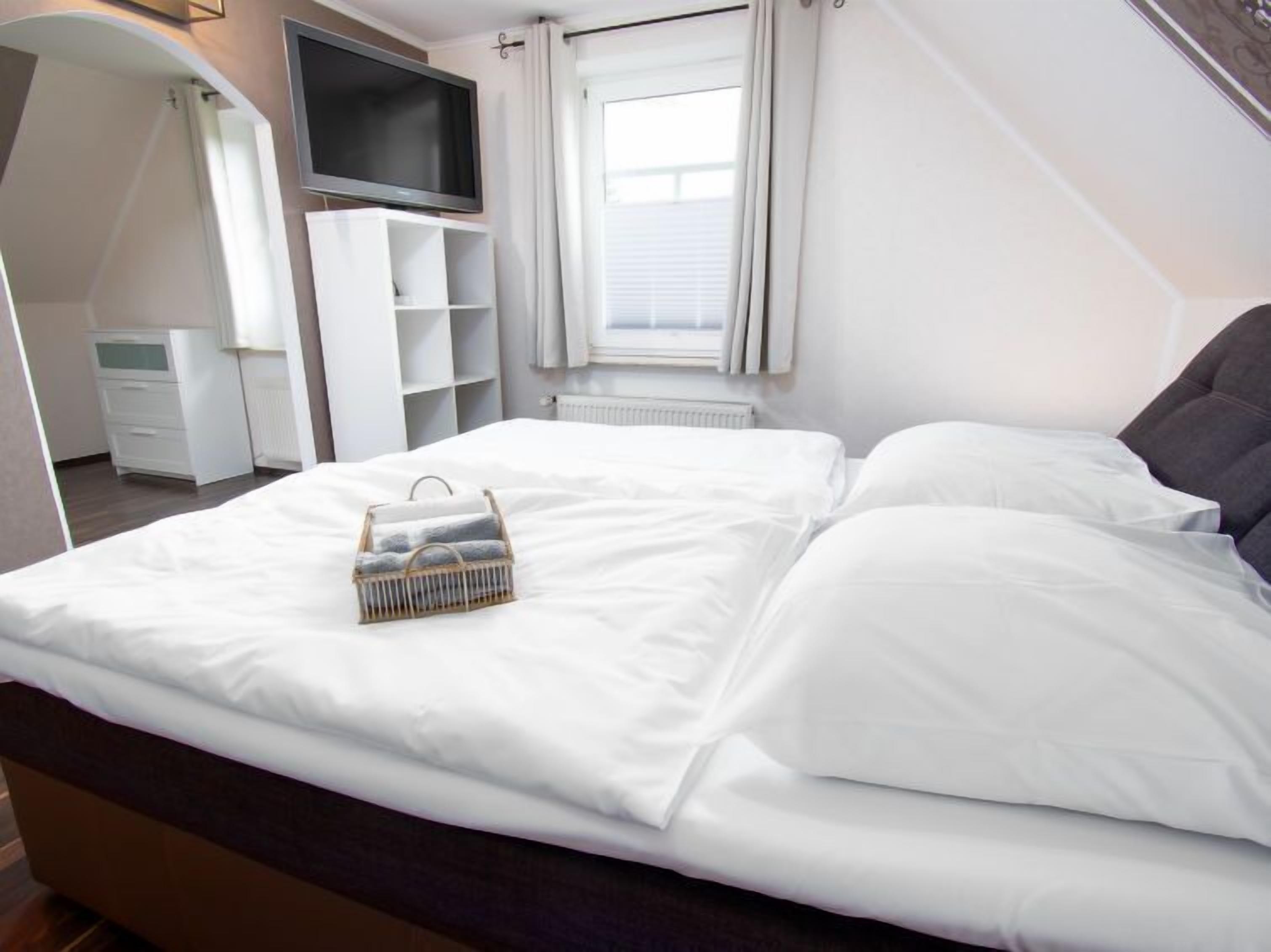 Een keurig opgemaakt bed met witte lakens en een klein mandje handdoeken.
