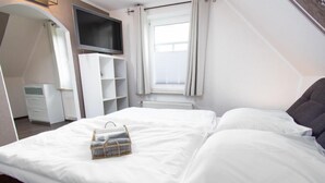 Een keurig opgemaakt bed met witte lakens en een klein mandje handdoeken.