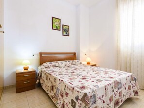 Un dormitorio con una cama de madera, dos mesitas de noche con lámparas, un pequeño aparador y dos cuadros enmarcados en la pared.