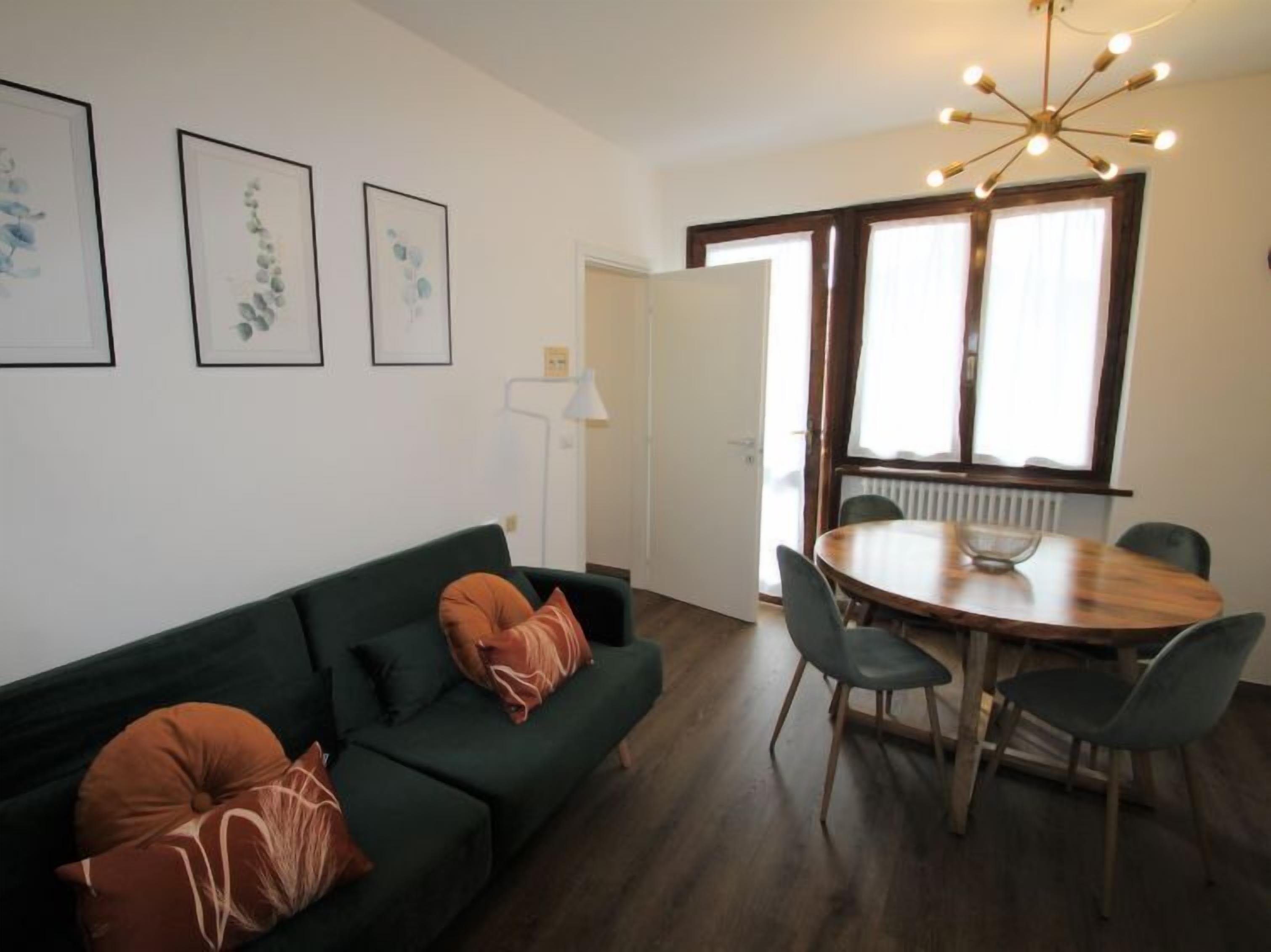A modern living space with a green sofa, a wooden dining table with chairs, and framed artwork on the wall.