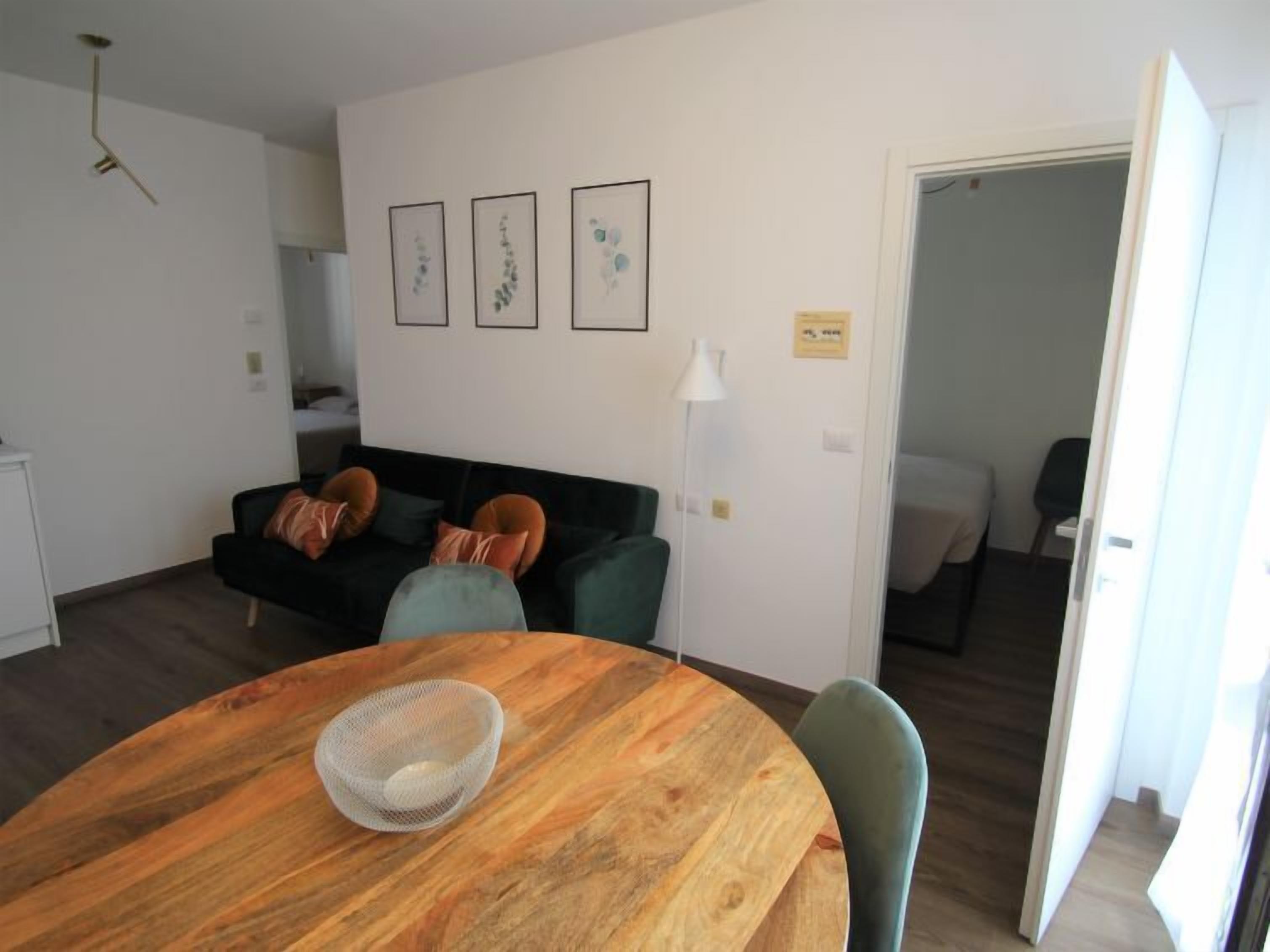 Een moderne woonkamer met een ronde houten tafel, een bank met kussens en een wand met ingelijste kunstwerken.