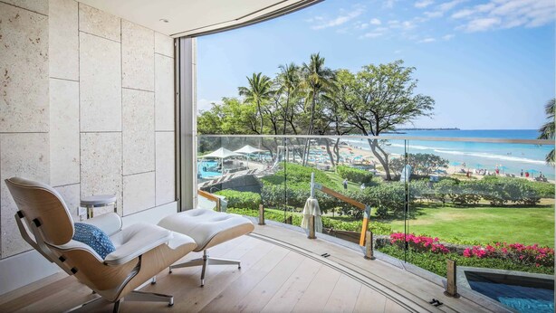 A modern room with a large glass window overlooking a beach and pool area.