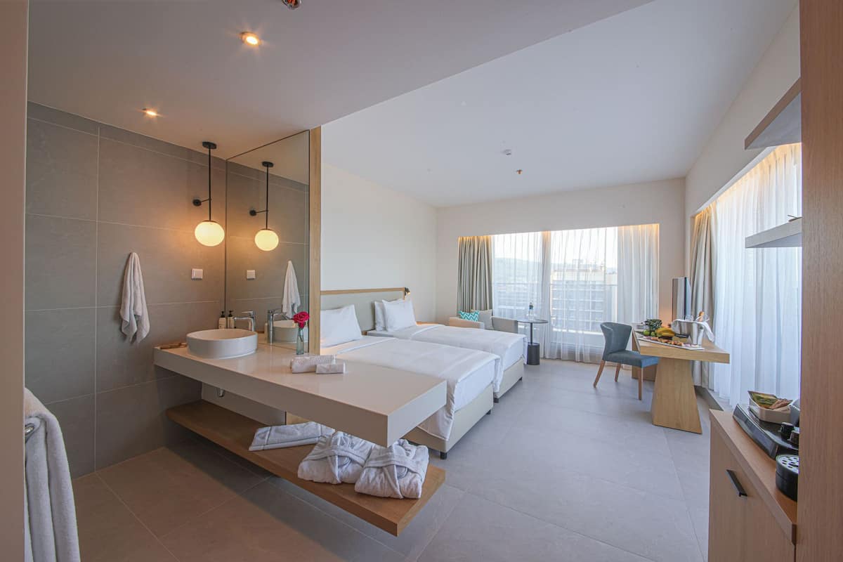 A modern hotel room with a large bed, a desk, a vanity with a mirror, and a bathroom with a sink and towel rack.