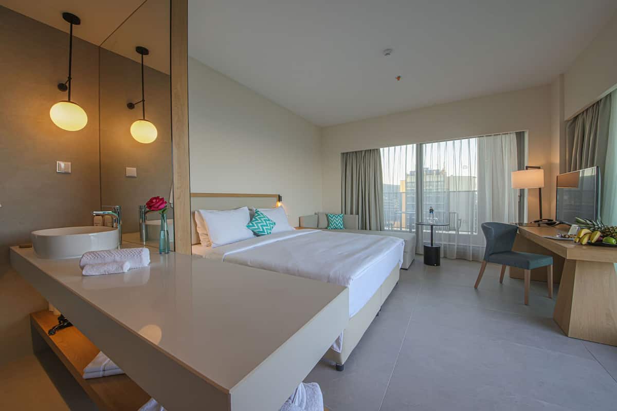 A hotel room with a large bed, a desk, a bathroom with a bathtub, and a city view.