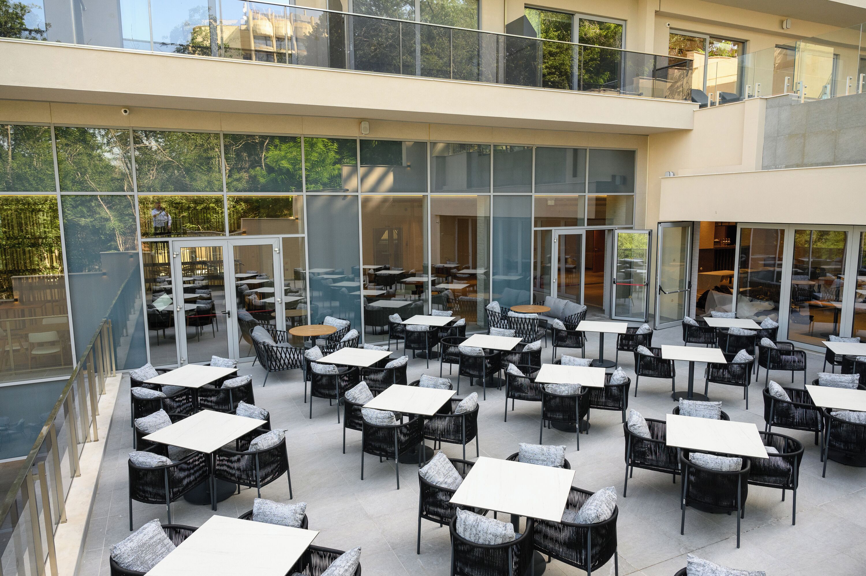 An outdoor café with multiple tables and chairs, large windows, and a glass railing.