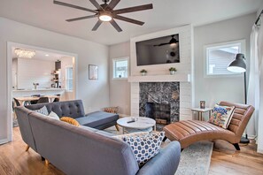 Una sala moderna con chimenea, ventilador de techo y un comedor visible al fondo.