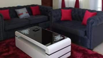 Un salon avec deux canapés sombres, une table basse blanche et un tapis rouge.