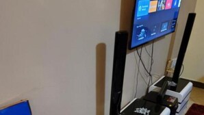 Ein Zimmer mit einem an der Wand befestigten Flachbildfernseher, einer weißen Unterhaltungsanlage, einem roten Feuerlöscher und einem Gemälde vom Eiffelturm.