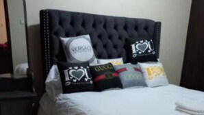 Ein Bett mit schwarzem Kopfteil, weißer Bettwäsche und mehreren Kissen mit Markenlogos.