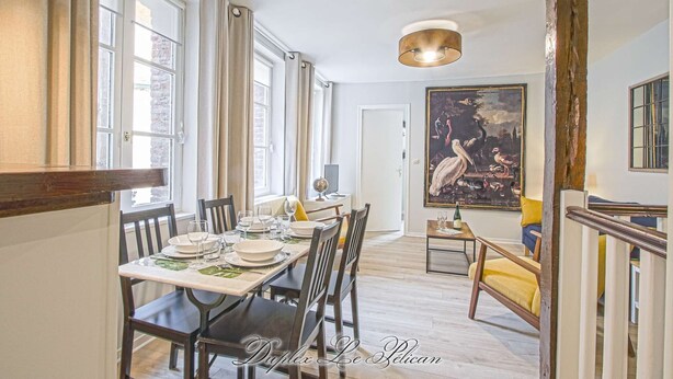 A dining area with a table set for four, a globe, and a bottle on the table. There is a large painting on the wall and a staircase to the right. - Super calm cosy & cute 2 bdr at the heart of Old Honfleur- Duplex Le Pélican ★★★★ (Honfleur)