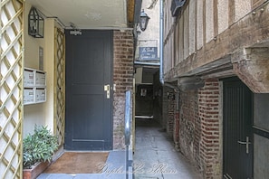 A narrow alleyway with a black door, a metal gate, and a brick building with a sign above the door.