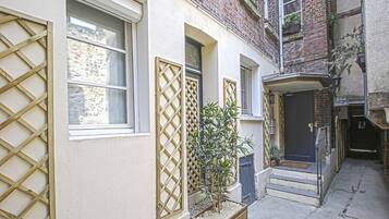 A narrow alleyway with a building featuring a wooden lattice window, a small potted plant, and a door with a sign.