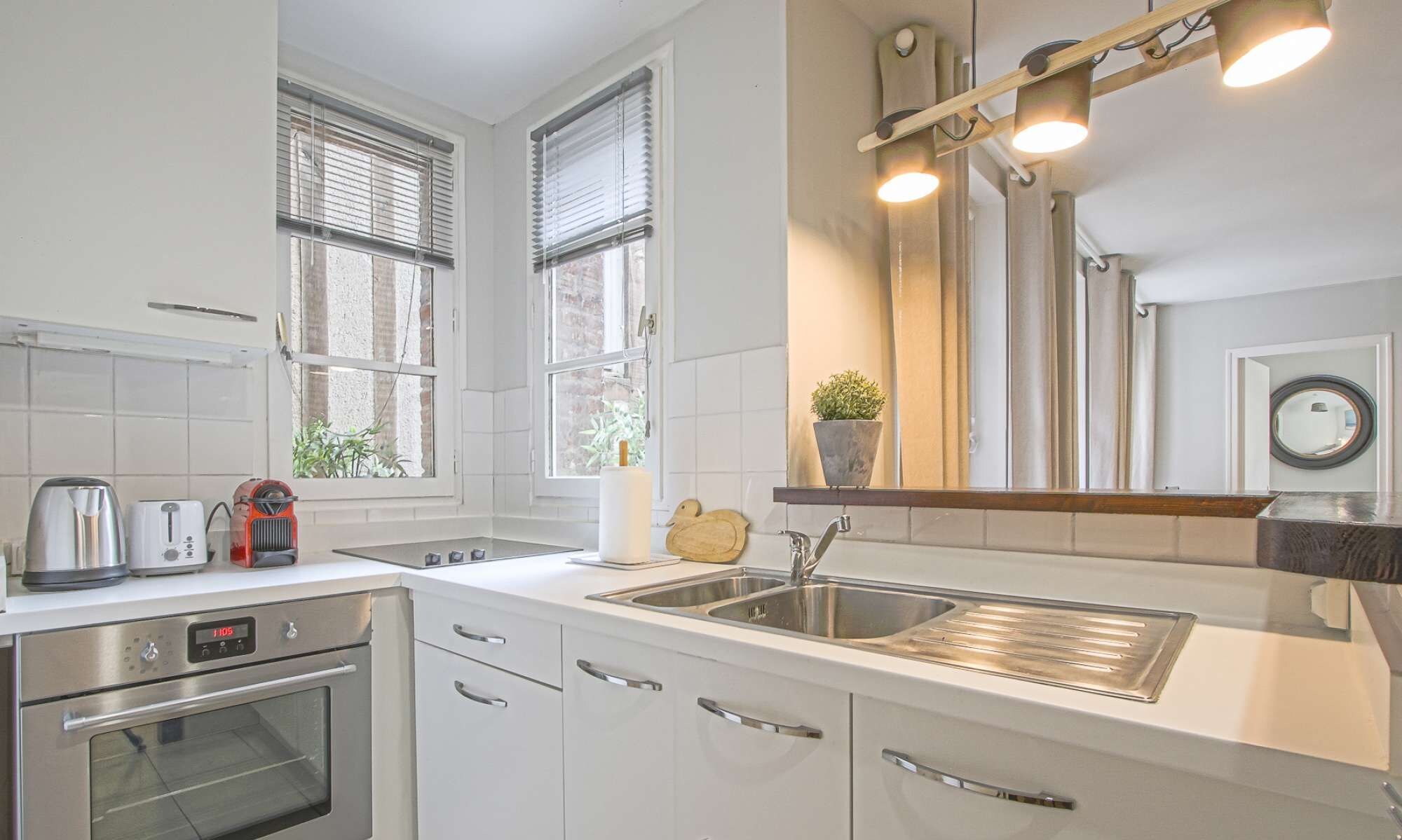 A modern kitchen with white cabinetry, stainless steel appliances, and a large window with blinds.