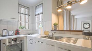 A modern kitchen with white cabinetry, stainless steel appliances, and a large window with blinds.